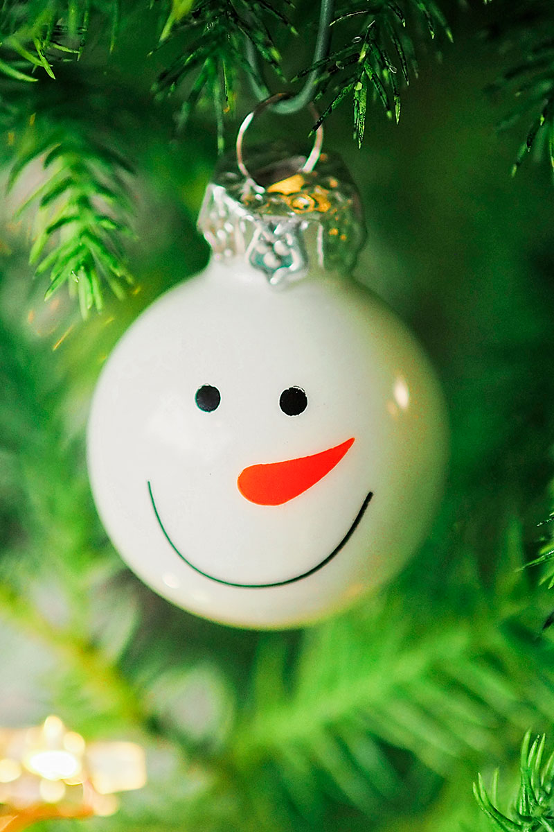 close up picture of a smiling snowman Christmas ornament on a tree