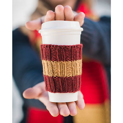 hands holding a travel coffee cup in a hand knit coffee cozy