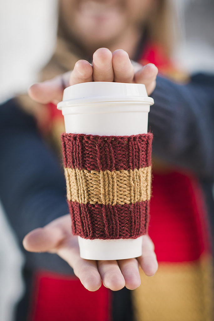 closeup of hands holding a travel coffee cup wearing a knitted coffee sleeve