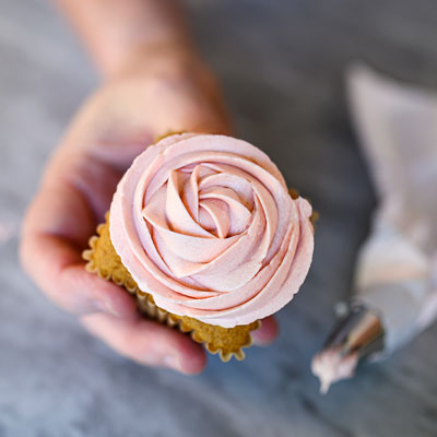 Hand holding a freshly piped cupcake in the design of a pink rosette