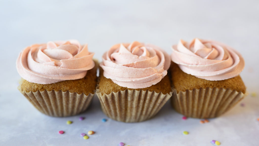 three cupcakes with pink frosting piped like roses