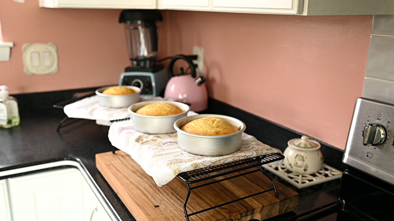 3 baked cakes in their pans cooling on racks