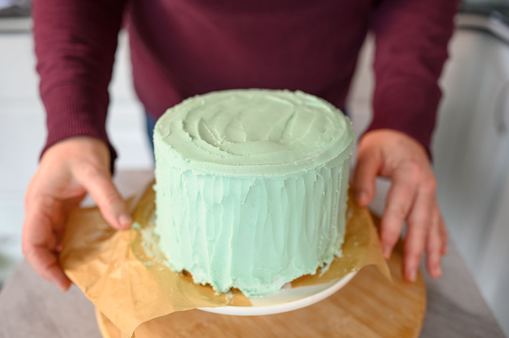 Mint green layer cake with person's hands on either side of the cake plate