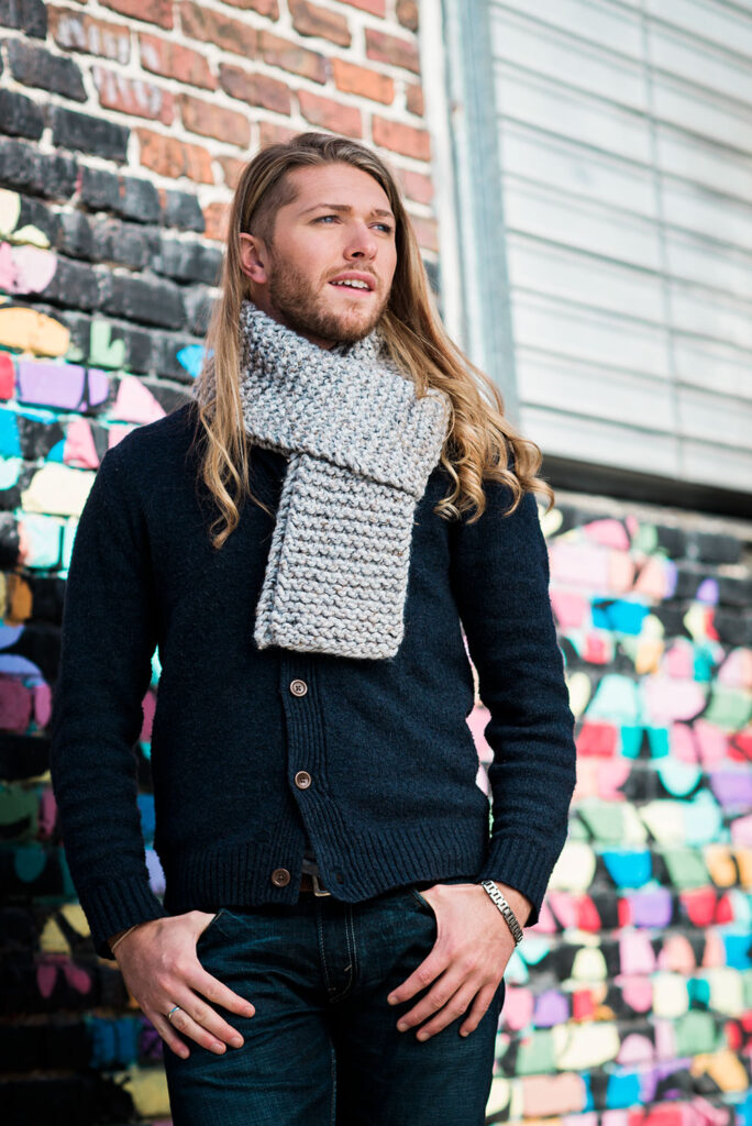 stylish young man demonstrates a wrapped scarf around his neck posing in from of a street art mural