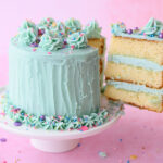 A large slice of 3 layer vanilla cake with the full cake frosted in mint green buttercream with spinkles