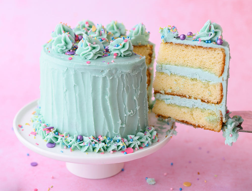 Vanilla layer cake with 3 layers of vanilla cake and frosted with mint green frosting. A slice has been taken to show the layers and is on the cake server