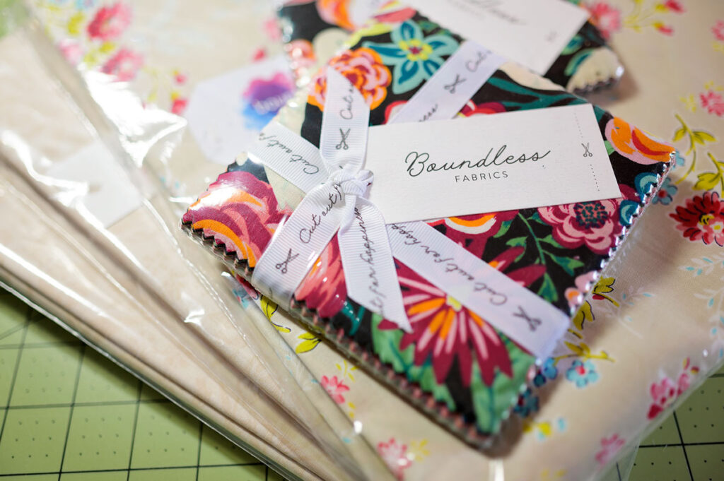 Overhead image of a stack of bright Charm Square fabric on a stack of neutral yardage.