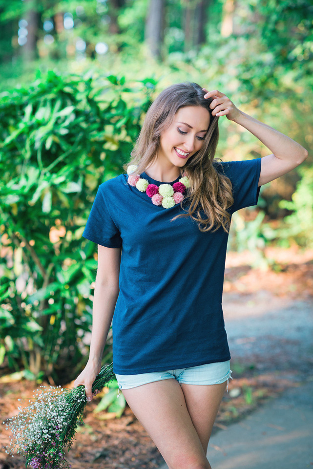 Smiling woman modeling a navy blue tshirt decorated with mulit color pom poms