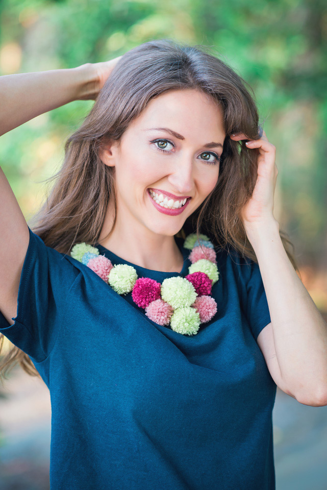 Smiling woman modeling a navy blue tshirt decorated with mulit color pom poms