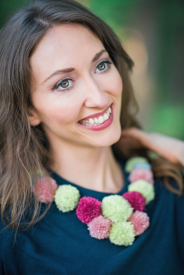 Smiling woman modeling a navy blue tshirt decorated with mulit color pom poms