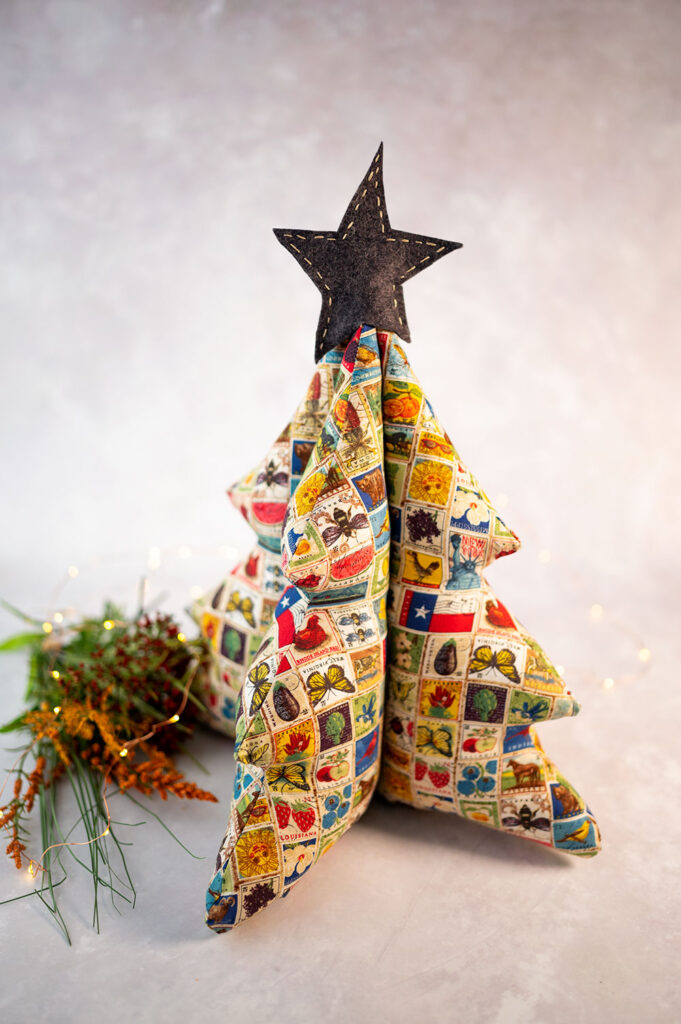 A table top fabric Christmas tree sewn in fabric that looks like vintage postage stamps posed with dried flowers and fairy lights