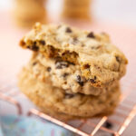 closeup of chocolate chip cookie with a bite taken out. Cookie is stacked on top of another and resting on a copper cooling rack.
