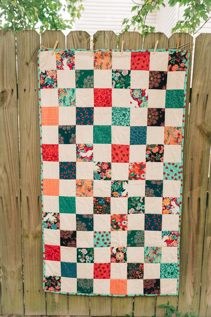 A patchwork finished quilt is displayed on a wooded fence.