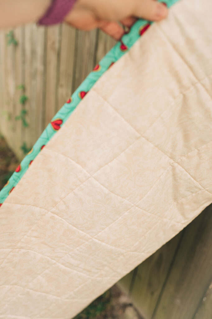 The backing of a finished quilt showing the binding and the quilted pattern on the backing fabric.