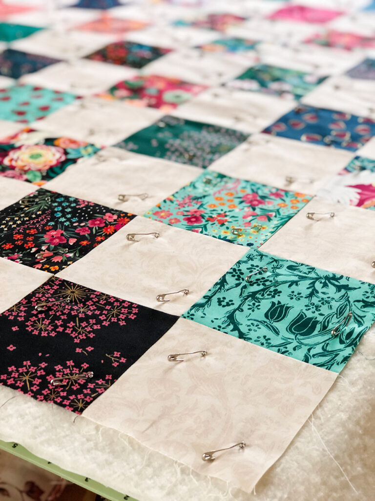 Closeup of a patchwork quilt that is pin basted to the batting and backing material.