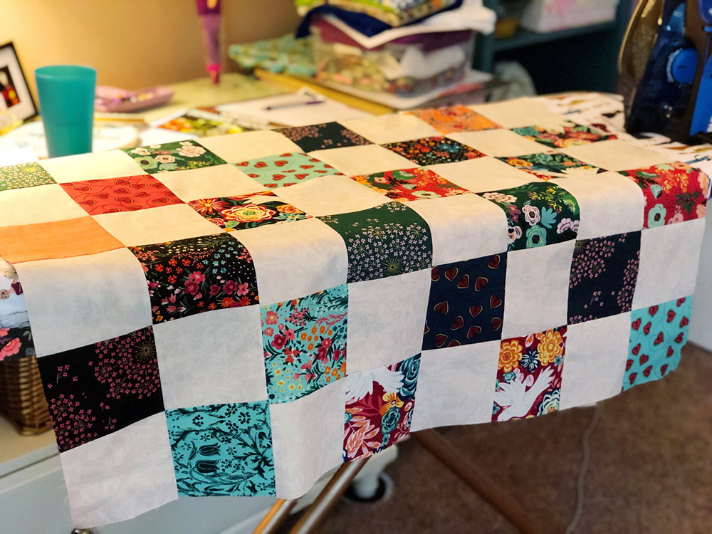 A partially sewn quilt top is spread across an ironing board.