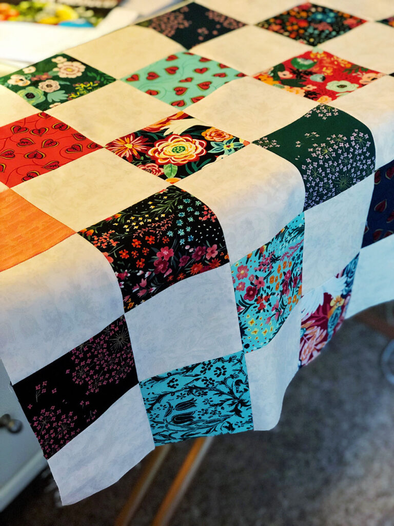 A partial quilt top in process of being pieced together is draped over an ironing board.