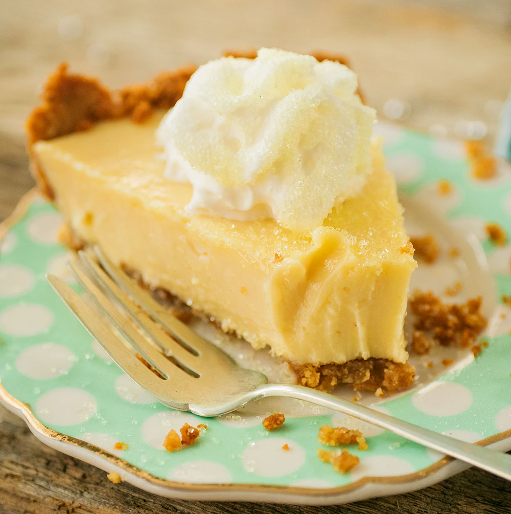 Closeup view of lemon pie topped with whipped cream, on a green polka dot plate with a bite taken out of the pie