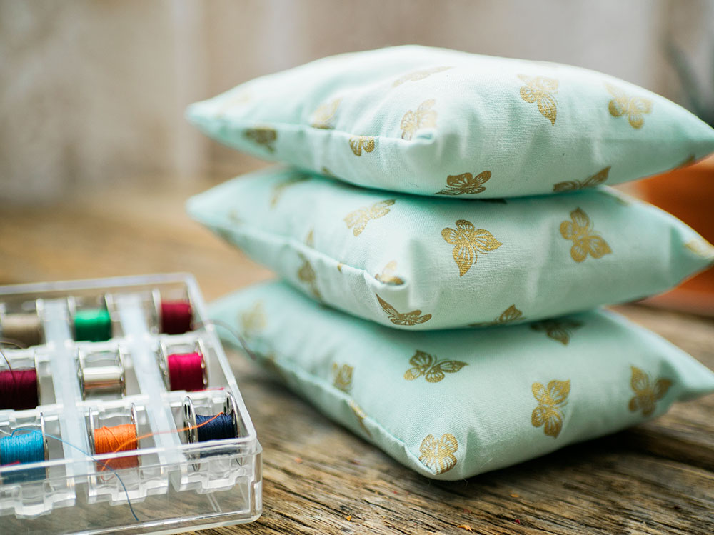 Three blue dream pillows stacked next to a case of bobbins with different thread colors