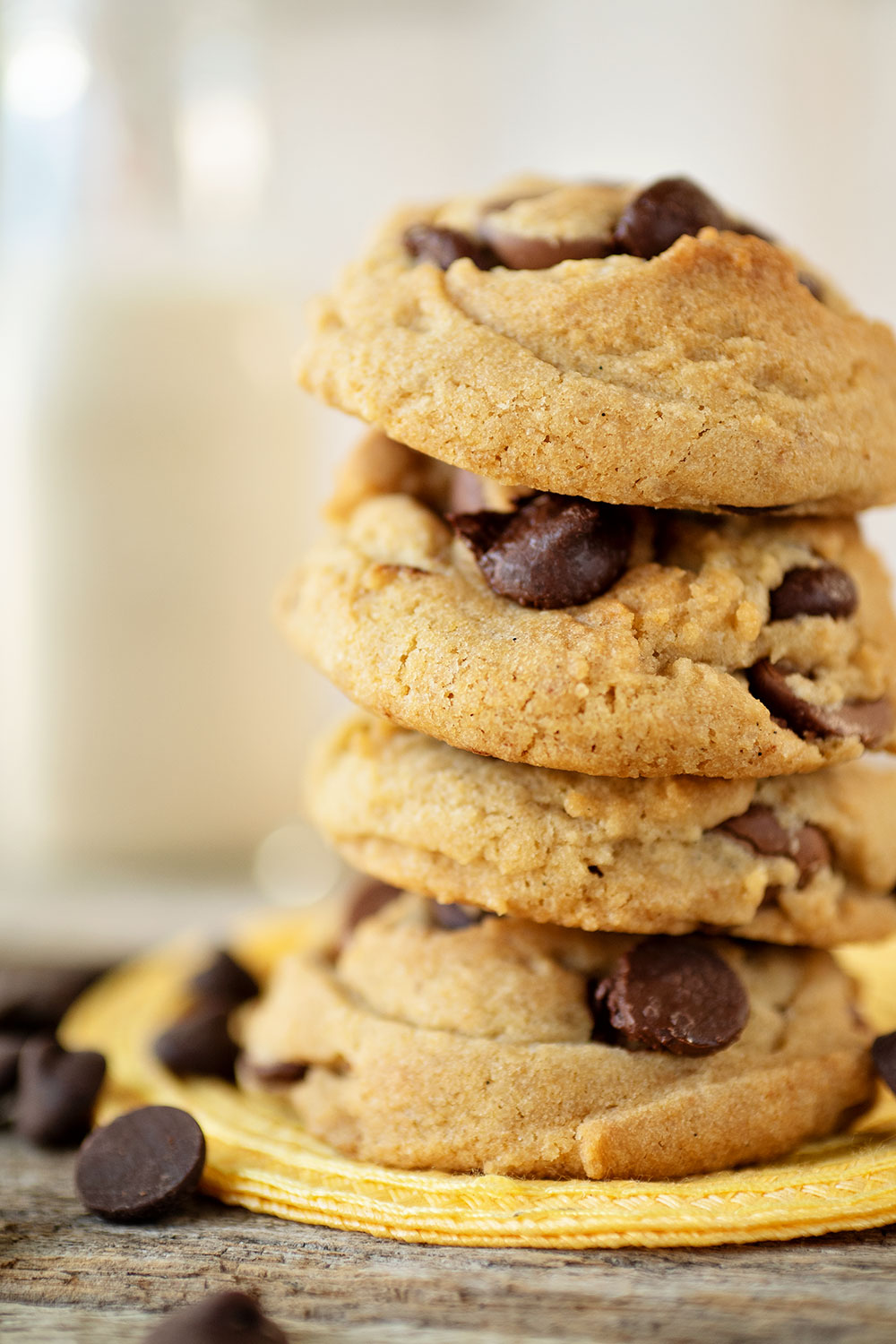 closeup view of 4 thick, soft baked vegan chocolate chip cookies on a yellow trivet with chocolate chips sprinkled everywhere