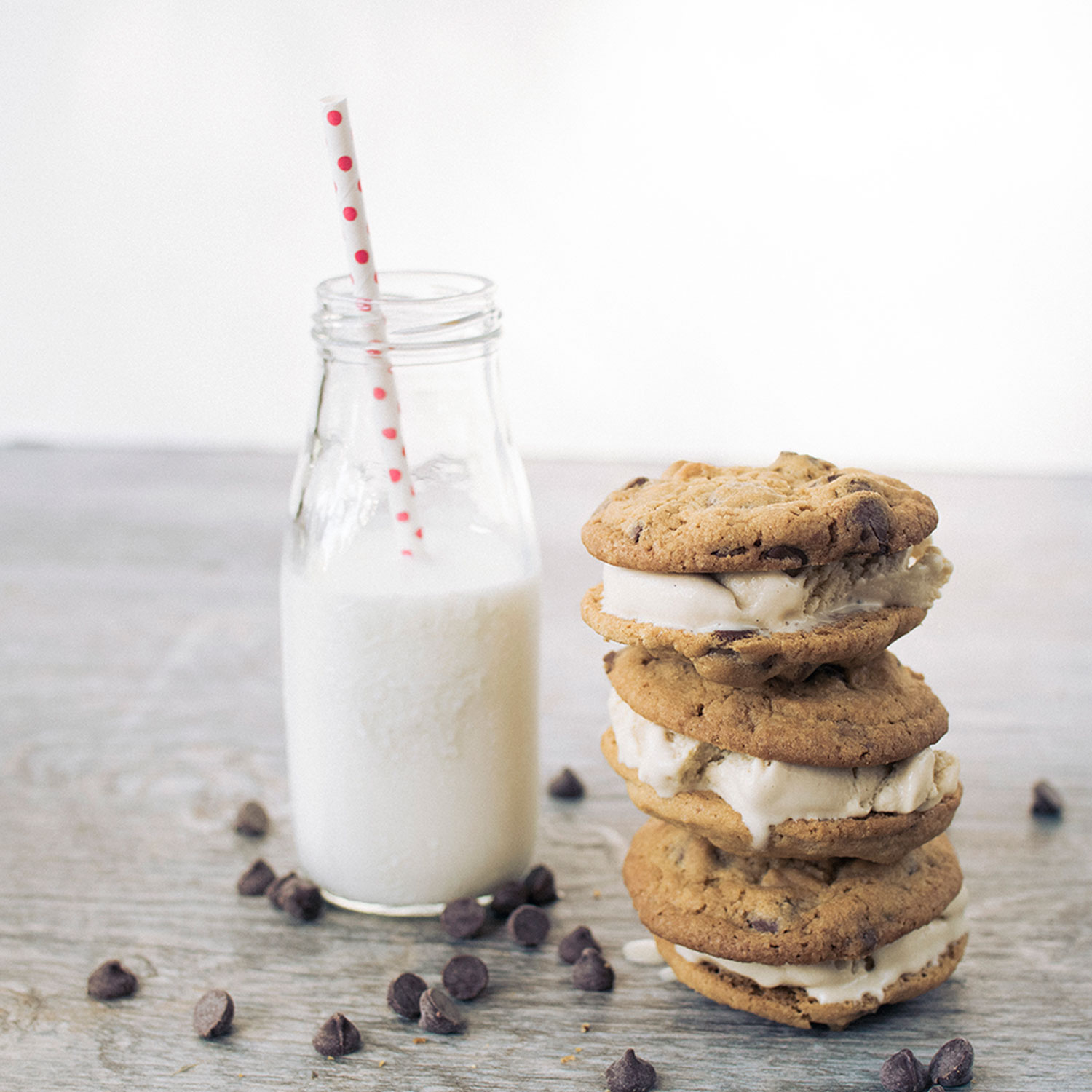 Stack of 3 ice cream sandwiches made with cookies and ice cream shown with a small milk bottle of milk and a pink polka dot straw