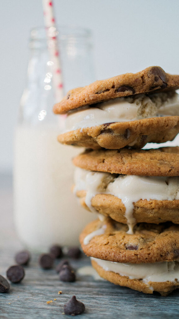 A tall stack if homemade cookie ice cream sandwiches. The ice cream is slightly melting and there are chocolate chips scattered around