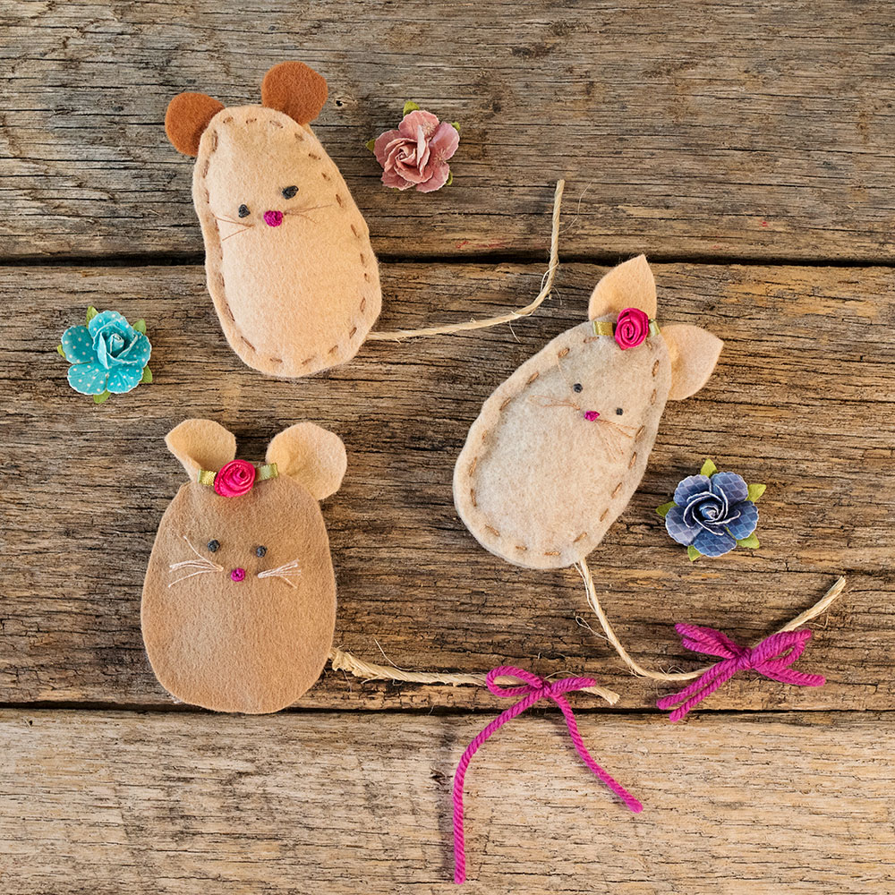 overhead view of a felt mouse family with a hand stitched faces posed next to paper roses