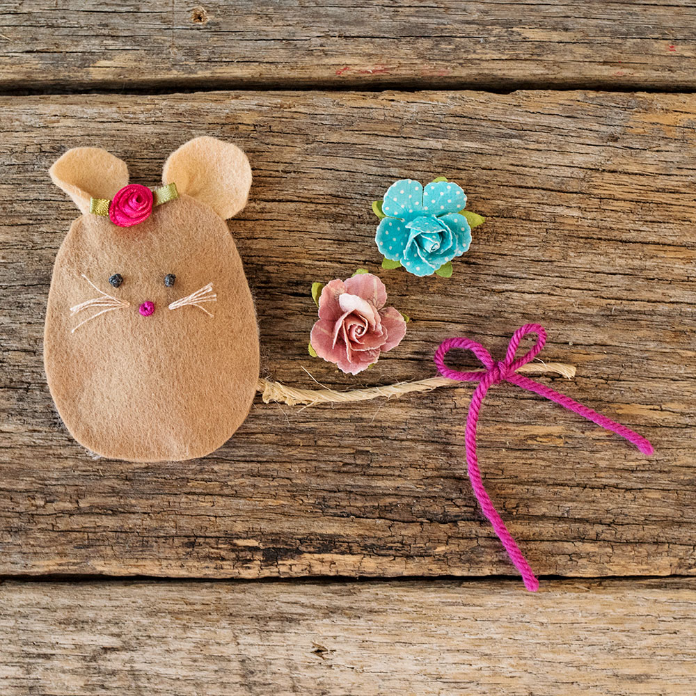 overhead view of a felt mouse with a hand stitched face posed next to paper roses