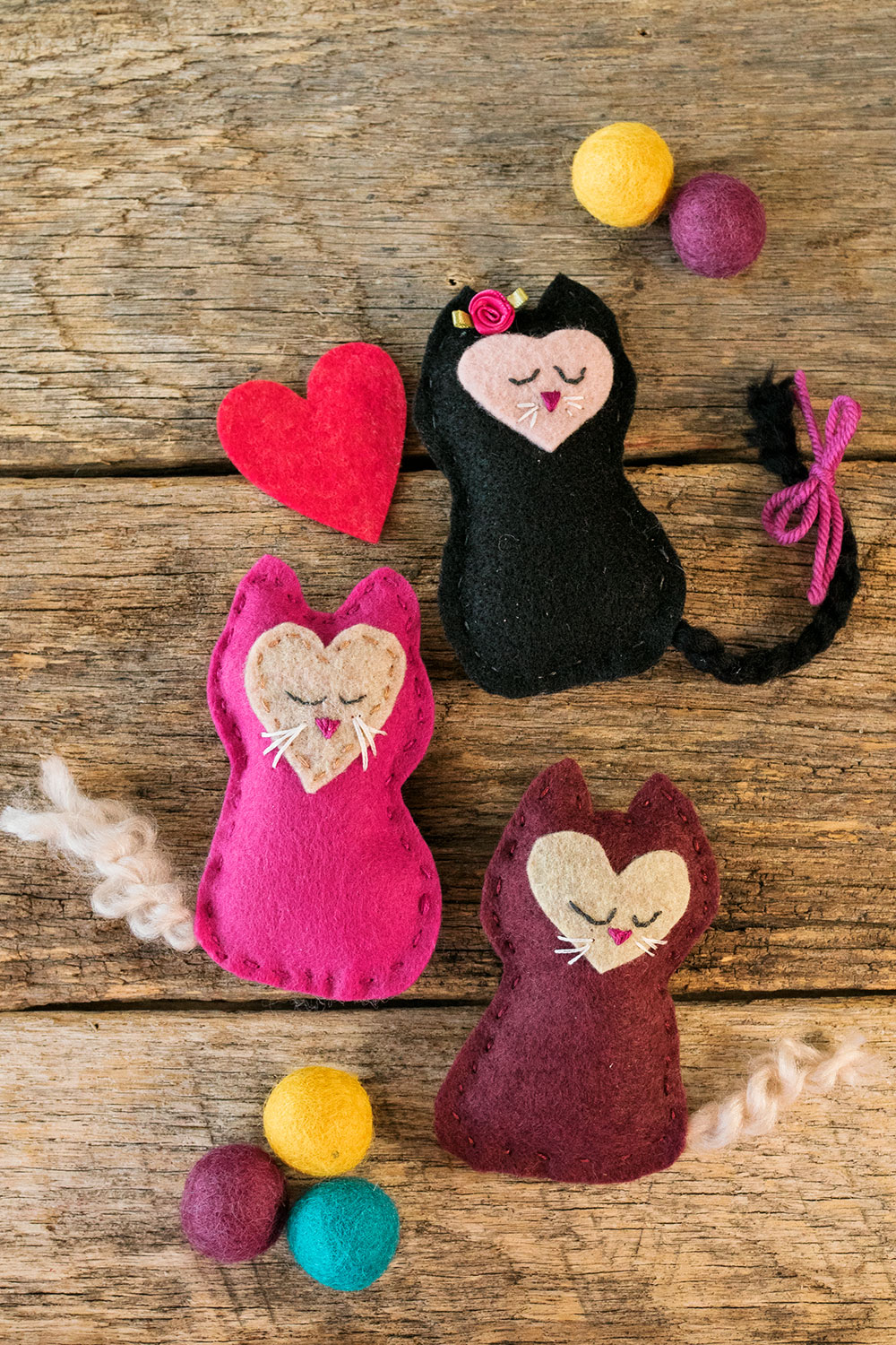 A collection of three small kitten toys hand sewn from felt posed with a felt heart and wool felted balls