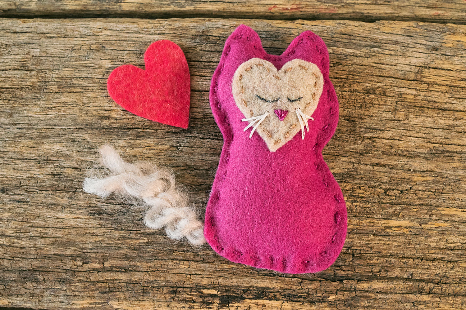 closeup of a handstitched felt kitten toy with a felt heart cut out