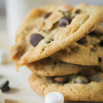 a stack of s'mores cookies with chocolate chips and marshmallows scattered around