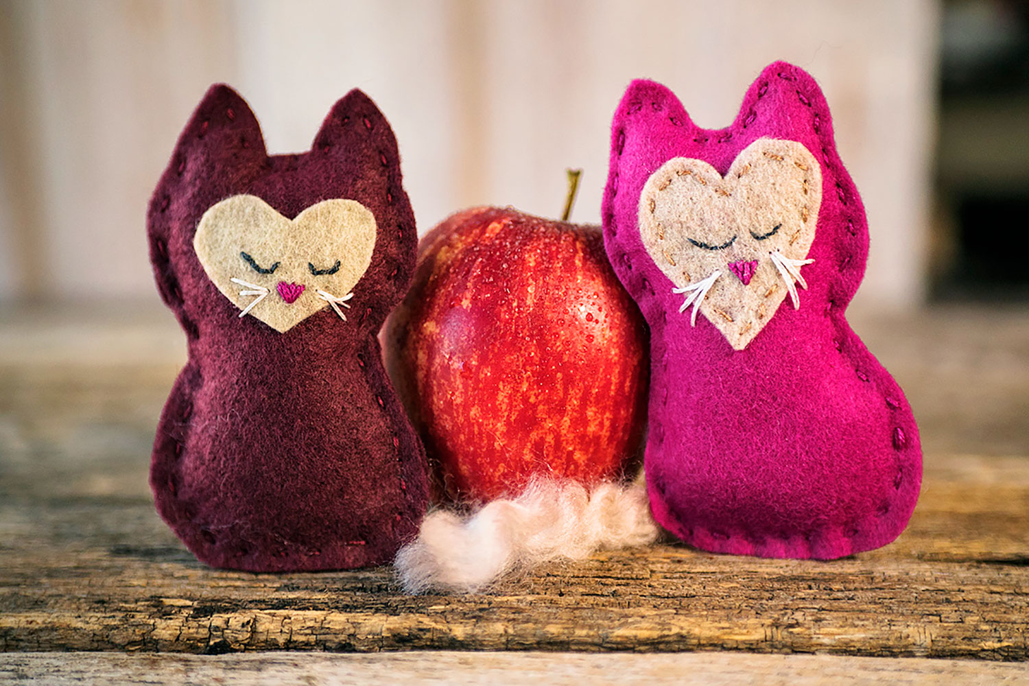 Two felt kitten toys posed with an apple. 