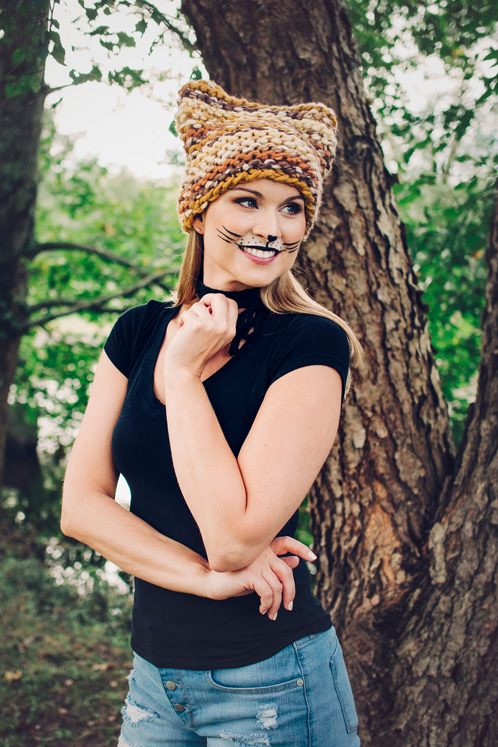beautiful blonde model wearing makeup to look like a cat in a brown and golden chunky knit hat with ears