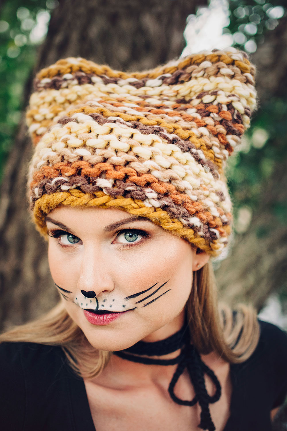 beautiful blonde model wearing makeup to look like a cat in a brown and golden chunky knit hat with ears