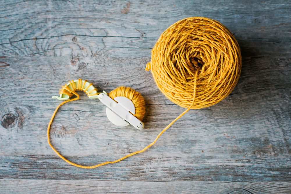 golden yellow yarn with a medium pom pom maker with yarn wrapped on the maker