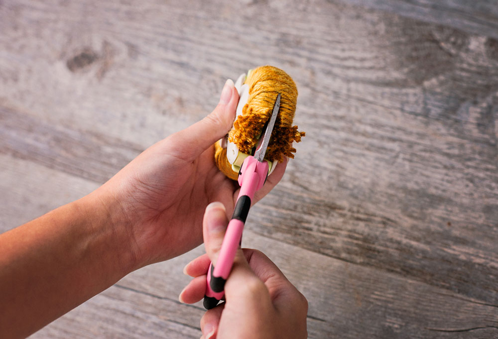 hands using scissors to cut wraps on a pom pom maker