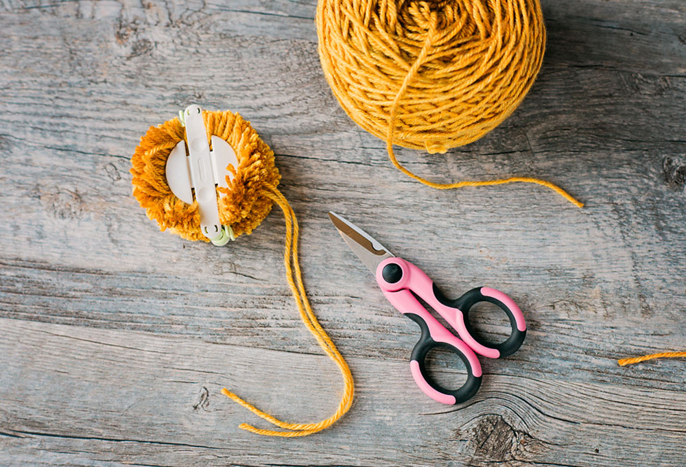 golden yellow yarn with a medium pom pom maker with fully cut yarn wraps and scissors