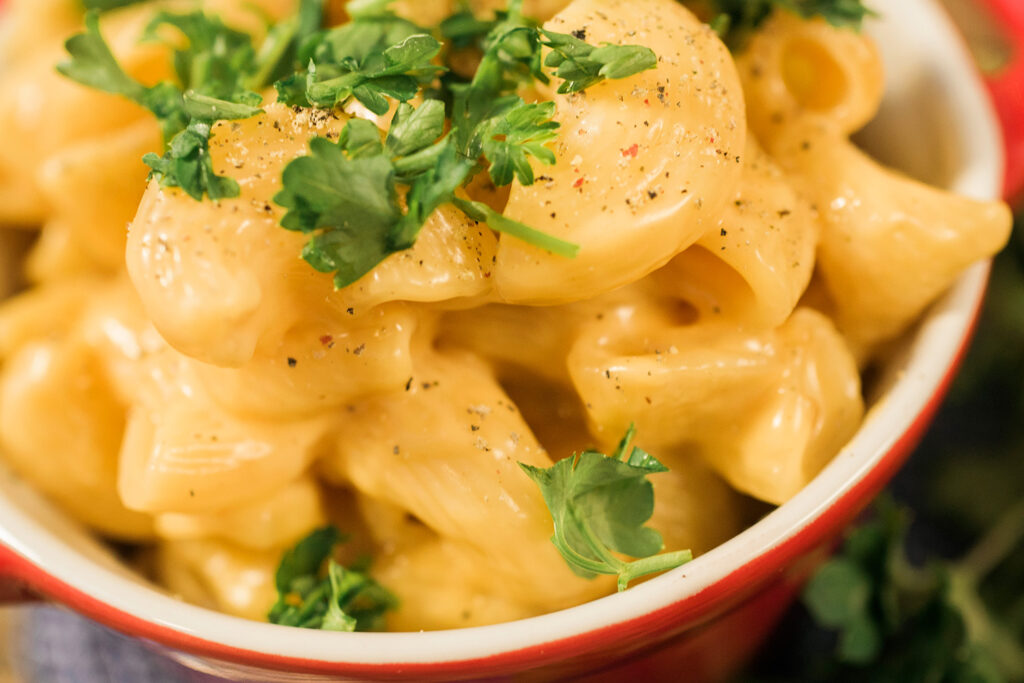 Close up view of a red dish filled with creamy golden macaroni and cheese garnished with chopped parsley