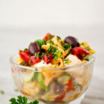 clear bowl with colorful tortellin salad with brigh green parsely scattered about