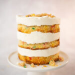 Side view of the a very tall layer cake frosted with fluffy, white frosting and decorated with a colorful rainbow crumb topping