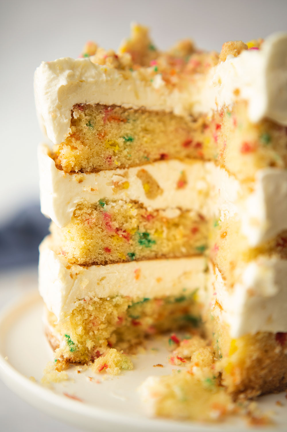 close up view of the sliced layer cake showing the rainbow sprinkle layers and fluffy white frosting.