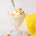 vintage glass dish with vanilla ice cream topped with multi colored toppings with yellow linen napkin and antique spoon