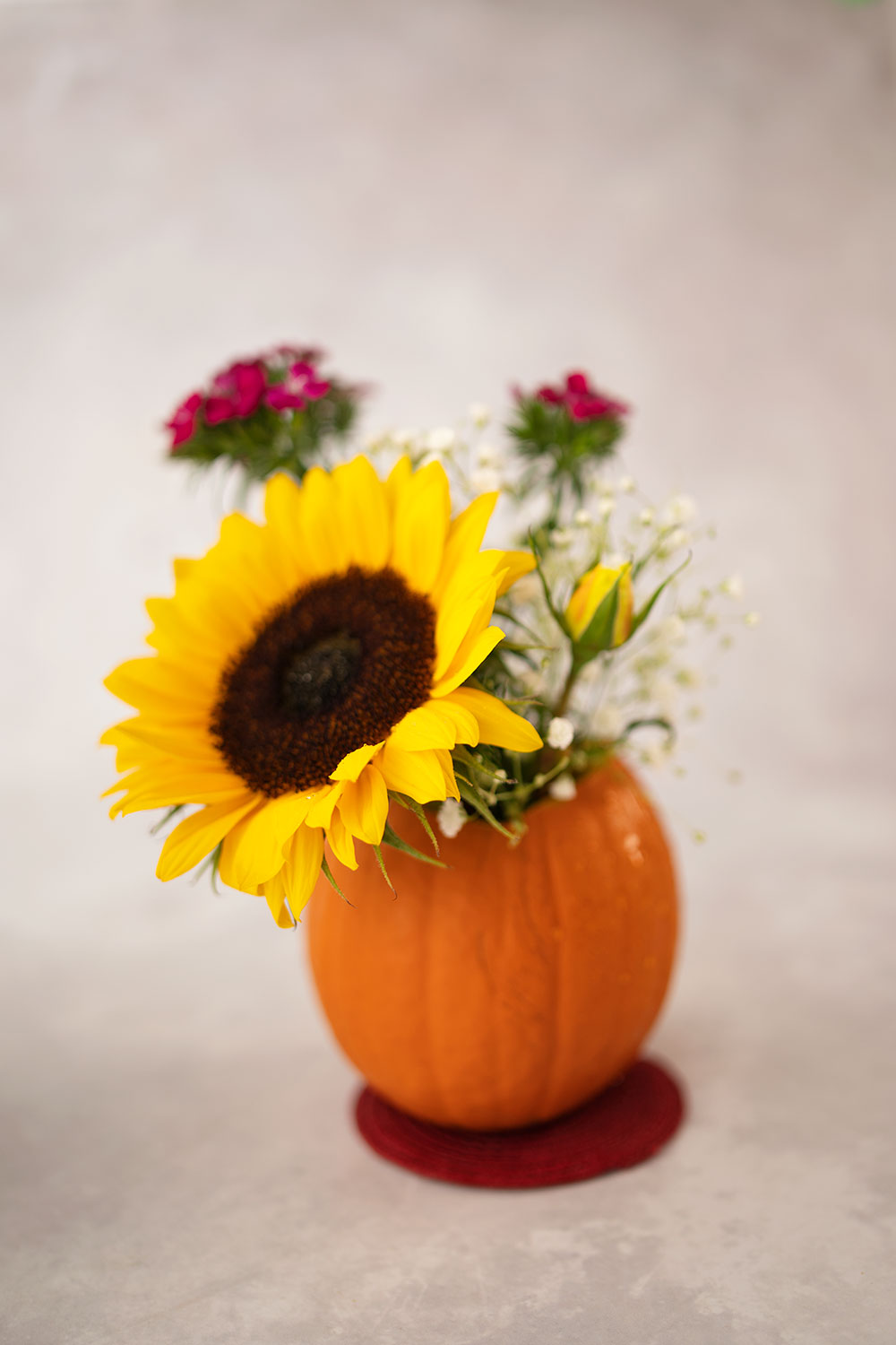 small pumpkin used like a vase and has a sunflower and a yellow rose with smaller flowers