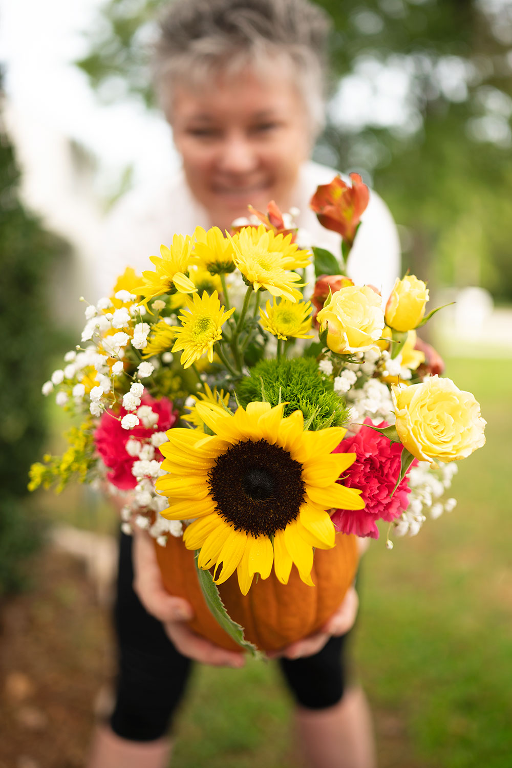 smiling woman holds a large pumpkin filled with fresh cut flowers in front of her