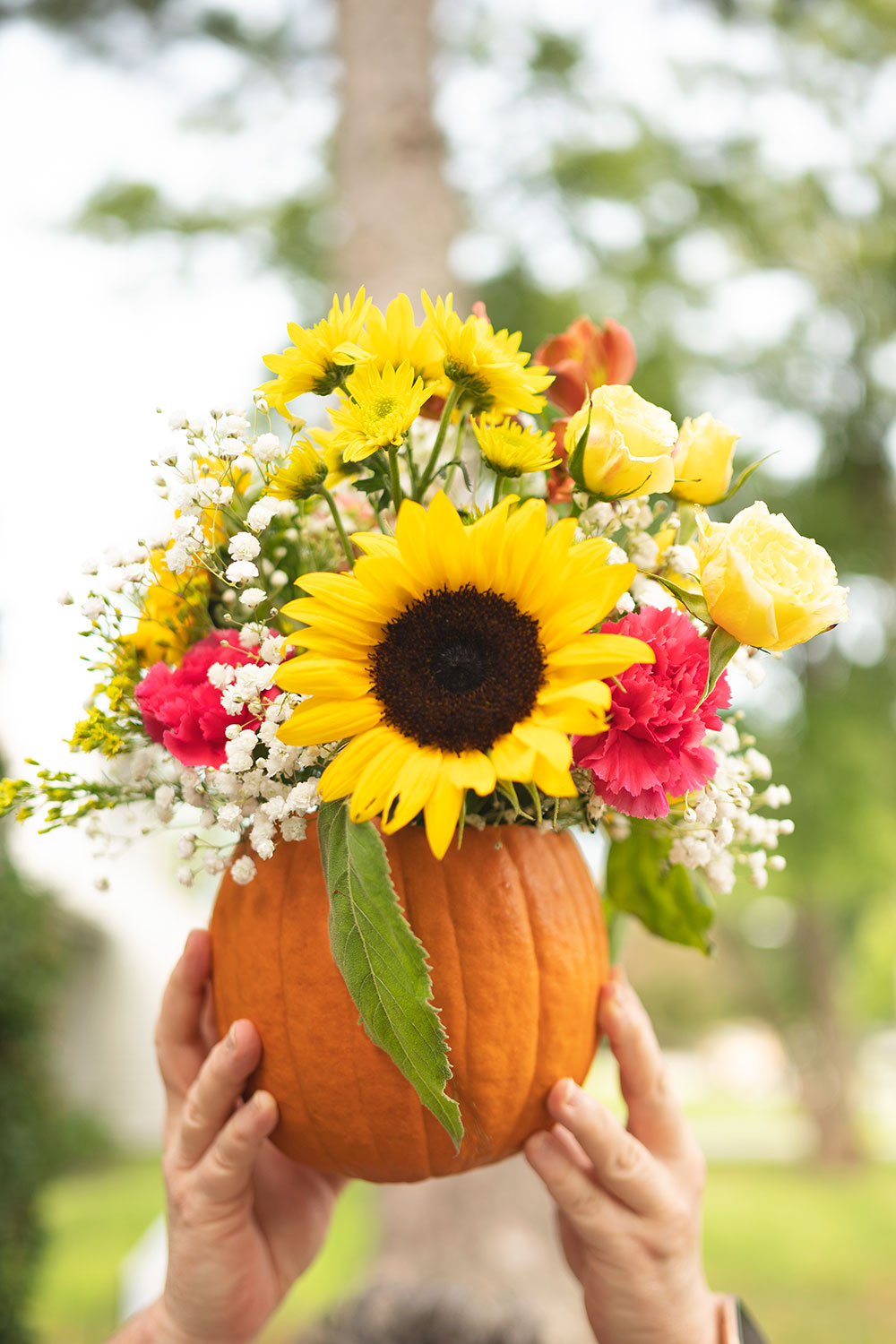 Hands holding a pumpkin with fresh flowers coming out its top