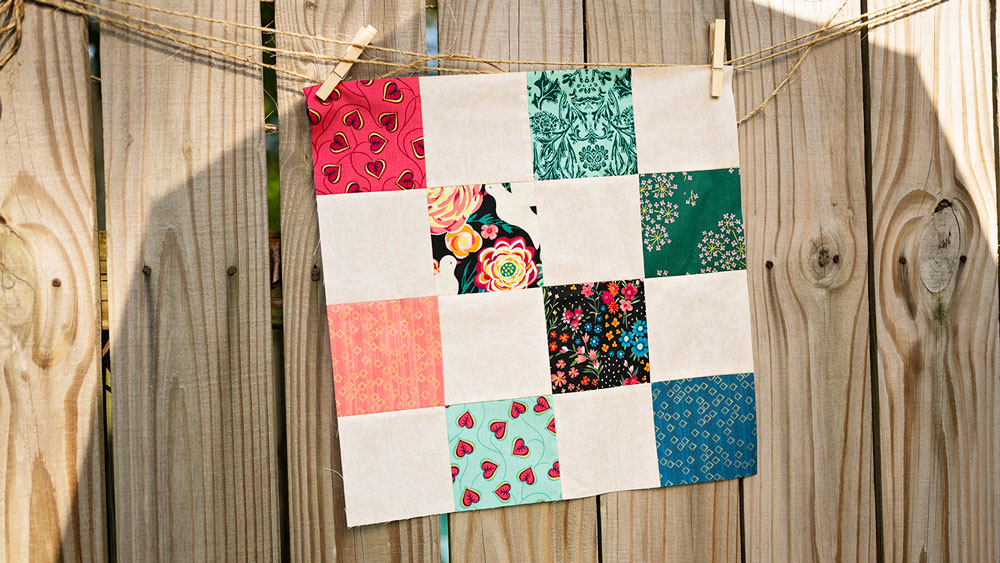 a small patchwork quilt hangs on a piece on twine on a rustic fence