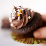 a hand holds a chocolate cupcake with the wrapper peeled back