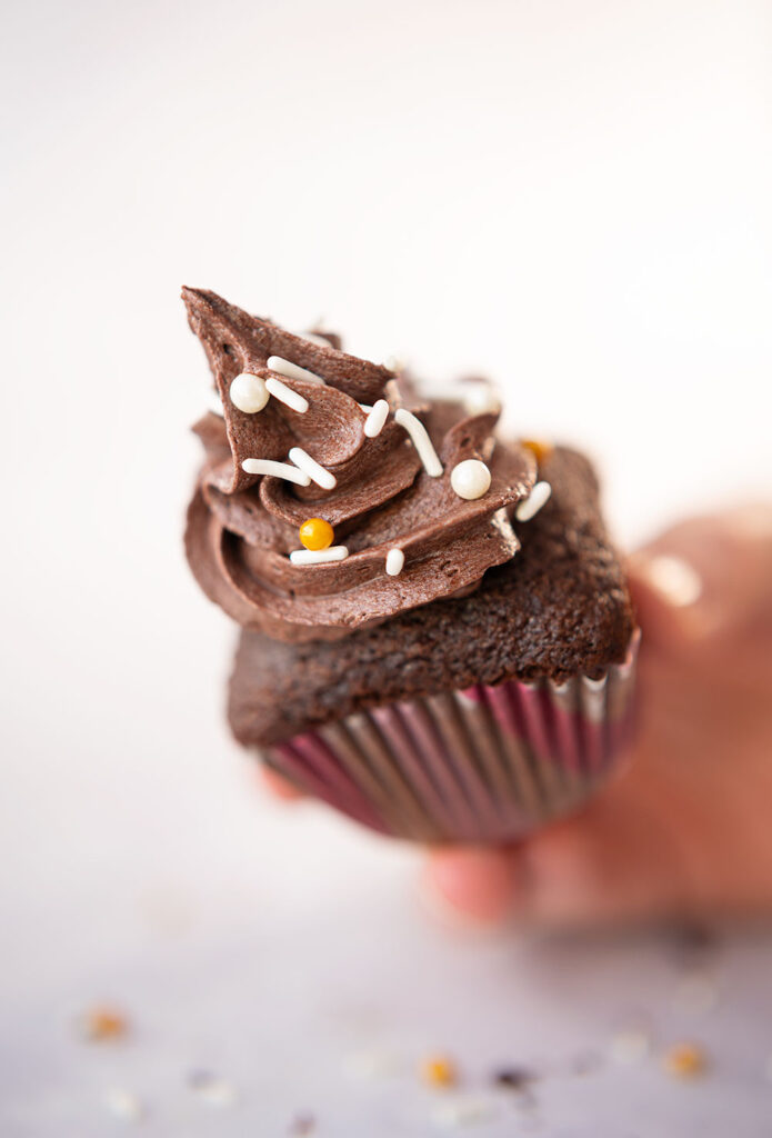 chocolate cupcake piped high with fudgy chocolate frosting held by a hand