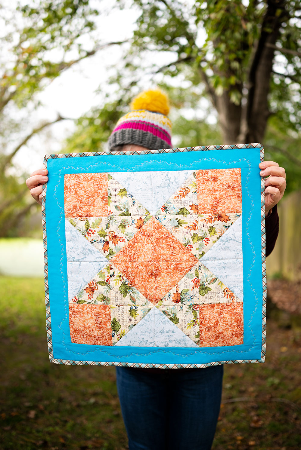 woman holds the completed mini quilt project showing off the ribbon star design