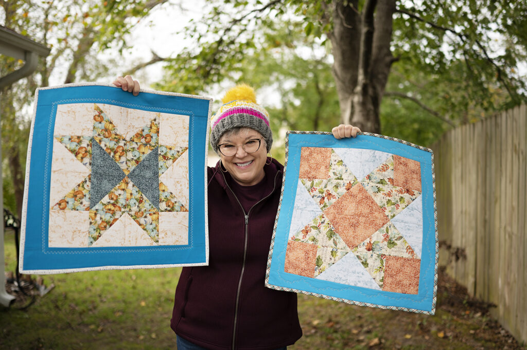 smiling woman holds two similar star block patterns